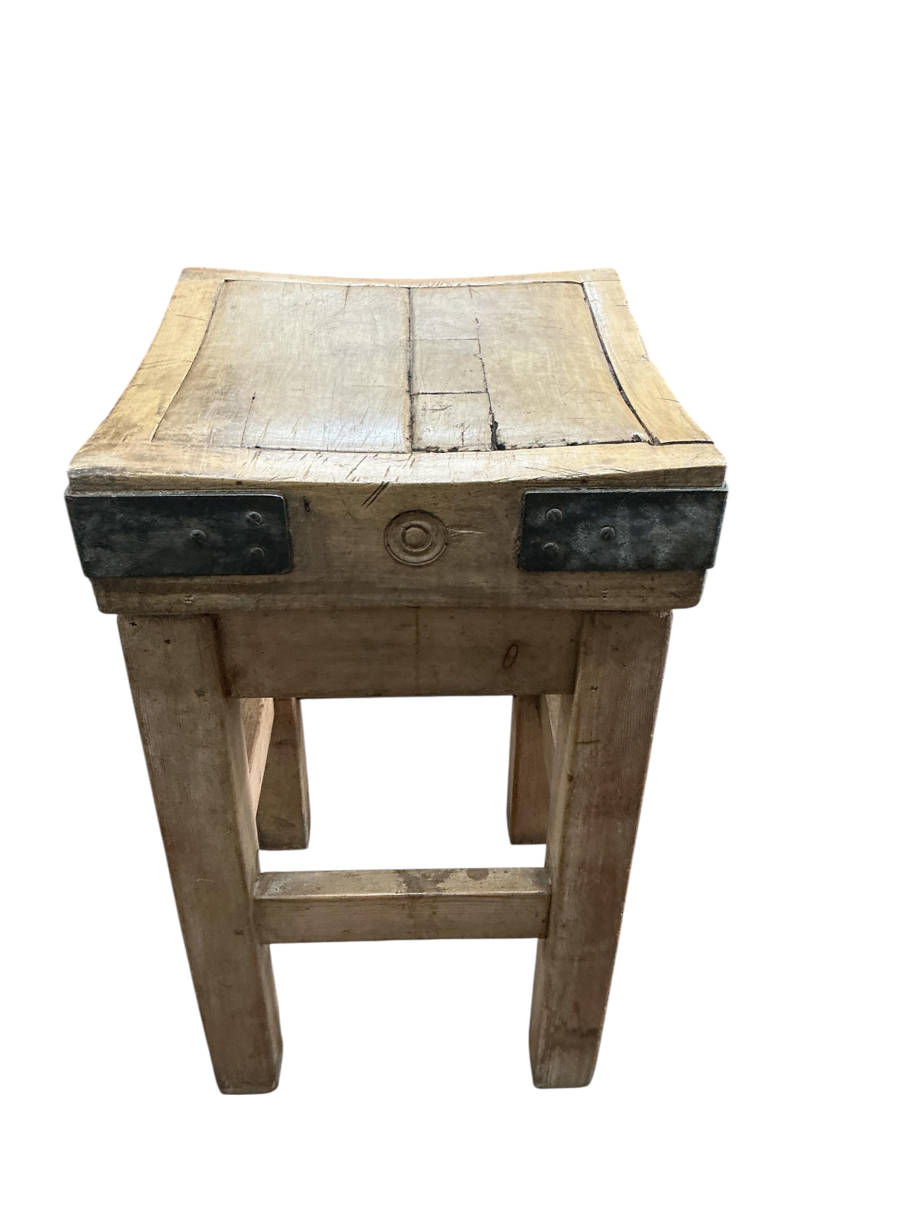 A small iron bound butcher’s block on stand bears metal plaque 